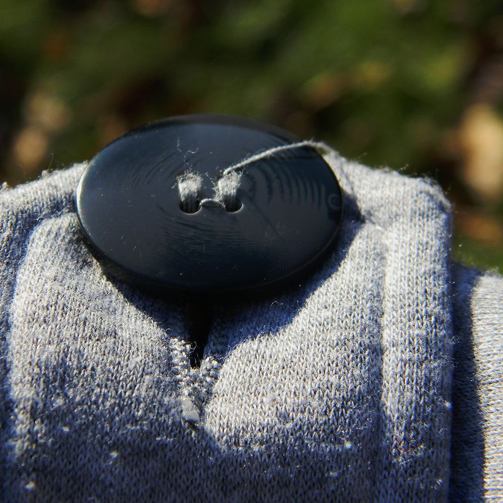 A dark button sewn onto a knitted wool garment